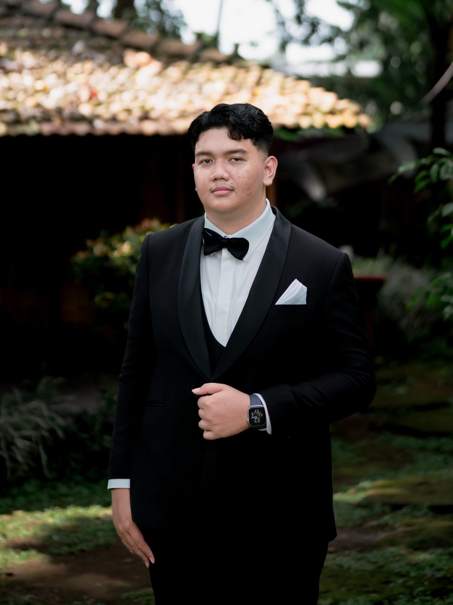 Rama Raihan in a black tuxedo and bow tie, standing in a garden